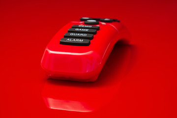 red plastic remote control with black rubber buttons with the text alarm, guard, game and demo