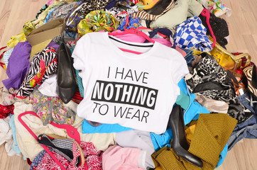Big pile of clothes thrown on the ground with a t-shirt saying nothing to wear. Close up on a untidy cluttered wardrobe with colorful clothes and accessories, many clothes and nothing to wear. - 95138202