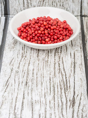 Pink peppercorn in a white bowl over wooden background