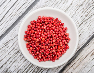 Pink peppercorn in a white bowl over wooden background