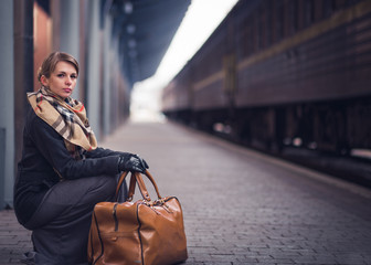 Young lonely sad blonde girl in a coat, gloves, a scarf and a skirt with a short haircut is waiting...