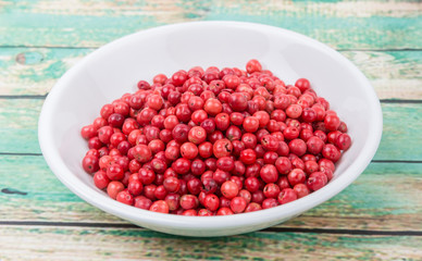 Pink peppercorn in a white bowl over wooden background