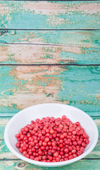 Pink peppercorn in a white bowl over wooden background