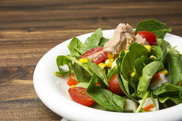 Fresh spinach salad with tuna and corn, small pieces of cherry tomatoes in white plate