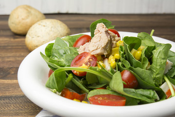 Fresh spinach salad with tuna and corn, small pieces of cherry tomatoes in white plate