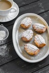 cookies madeleines with powdered sugar on oval plate on a light wooden surface