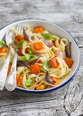 Pasta with baked pumpkin and onion on a white enamel plate on wooden surface