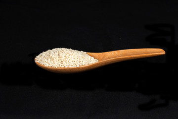 Sesame seeds in wood cup on black background