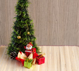 Santa Claus doll against a Christmas tree with gift box on wood