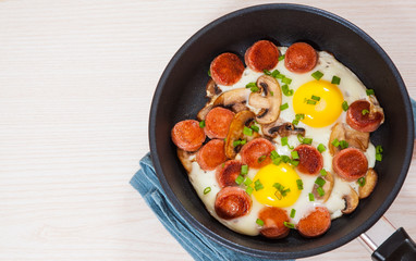 fried eggs with mushrooms and sausage in a frying pan