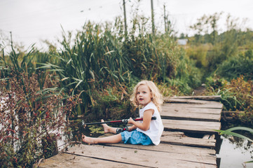 Naklejka premium lonely little child fishing from wooden dock on lake