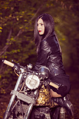 Obraz na płótnie Canvas Biker girl in a leather jacket on a motorcycle posing in nature