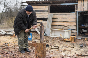 Old Ukrainian peasant choping firewood with an axe