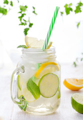 Lemonade with ice, lemon and lime slices in jar, straw.
