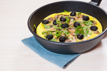 omelet with mushrooms, and olives in a frying pan