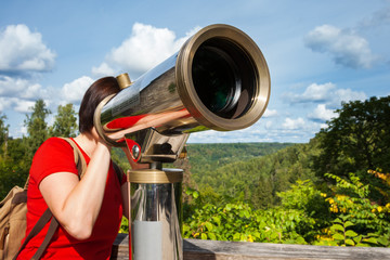 Young woman looking through tourist telescope, exploring landsca