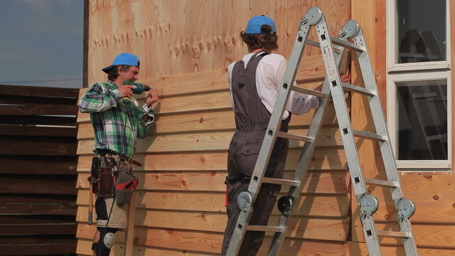 Work on Installing Siding/Standing on a stairs, carpenter fixes the siding on the house