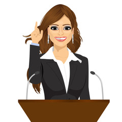 female orator standing behind a podium with microphones