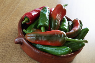 red and green peppers in a bowl of mud on a wooden table