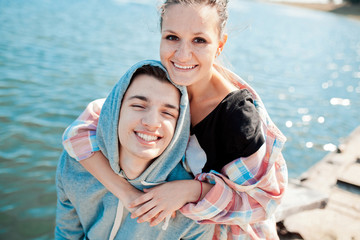 Fototapeta na wymiar Lifestyle. Feelings. Love. Portrait of two happy young people dating, hugging and smiling by a lake on a pier on a warm autumn day.