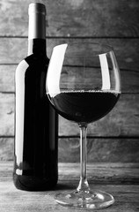 Bottle of red wine and a glass on wooden table,  black and white retro stylization