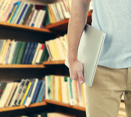 Male hand holding laptop on bookshelves background