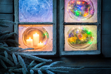 Beautiful burning candles for Christmas in frozen window at night