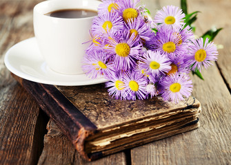 Old book with beautiful flowers and cup of tea on wooden table close up