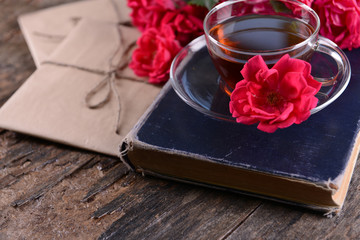 Old book with beautiful flowers and cup of tea on wooden table close up