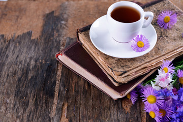 Old books with beautiful flowers and cup of tea on wooden table close up
