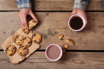 Female hands holding cup of coffee and cookies on wooden table close up