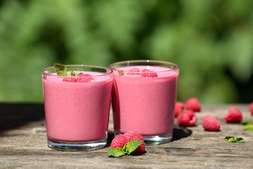 Glasses of raspberry milk shake with berries on bright background