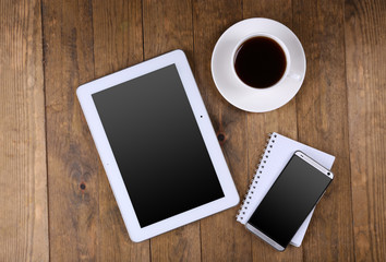 Blank tablet and mobile phone with notebook and cup of coffee on wooden background