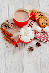 
winter mood , cocoa with marshmallows in a red cup , cinnamon and cookies with chocolate on a wooden background