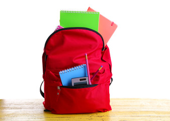 Red bag with school equipment on wooden table isolated on white