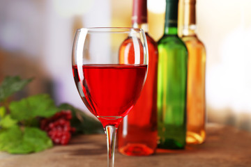 Red wine glass with colourful bottles on wooden table against unfocused background