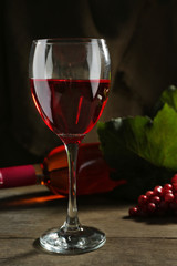 Red wine glass against wicker basket with grape and wine bottle on wooden table