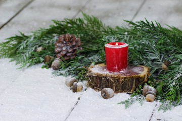 Red candle on log by garland and winter background