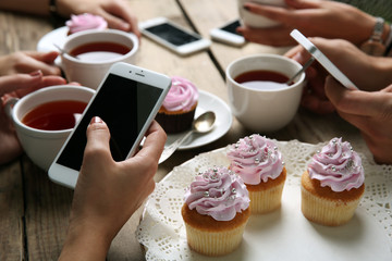 Four hands with smart phones holding  cups with tea, on wooden table background