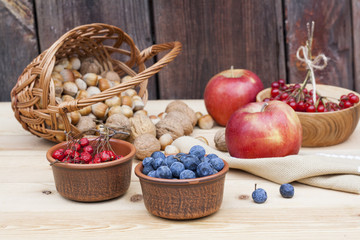 Autumn still life with walnuts and hazelnuts in the basket and autumn berry and vegetables on old...