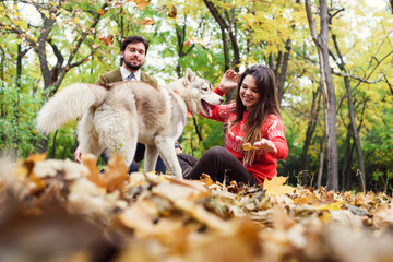 young happy couple in autumn park with husky dog