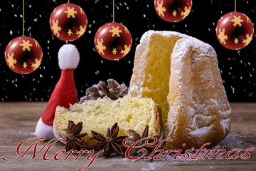 pandoro cake on wood with christmas balls, snowflake, cap and merry christmas written