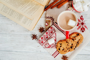 Naklejka na ściany i meble winter mood , cocoa with marshmallows in a red cup , cinnamon and cookies with chocolate on a wooden background
