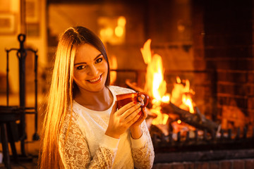 Woman drinking hot coffee relaxing at fireplace.