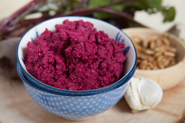 Beetroot pesto in a blue bowl on a wooden table with garlic, beetroot on the back, selective focus
