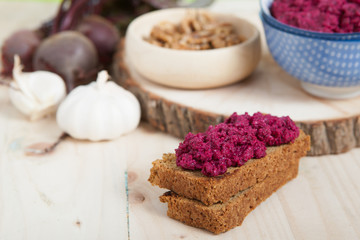Beetroot pesto in a blue bowl on a wooden table with garlic, beetroot and almond bread, selective focus