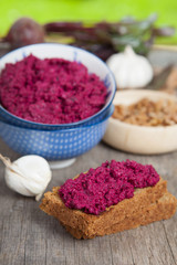 Obraz na płótnie Canvas Beetroot pesto in a blue bowl on a wooden table with garlic, beetroot and almond bread, selective focus