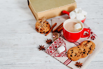 
winter mood , cocoa with marshmallows in a red cup , cinnamon and cookies with chocolate on a wooden background