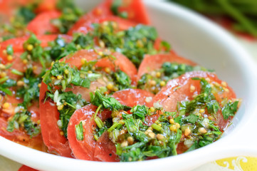 Tomato salad with marinade from mustard and green herbs on white plate.