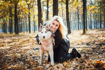 young beautiful female having fun with siberian husky in autumn park